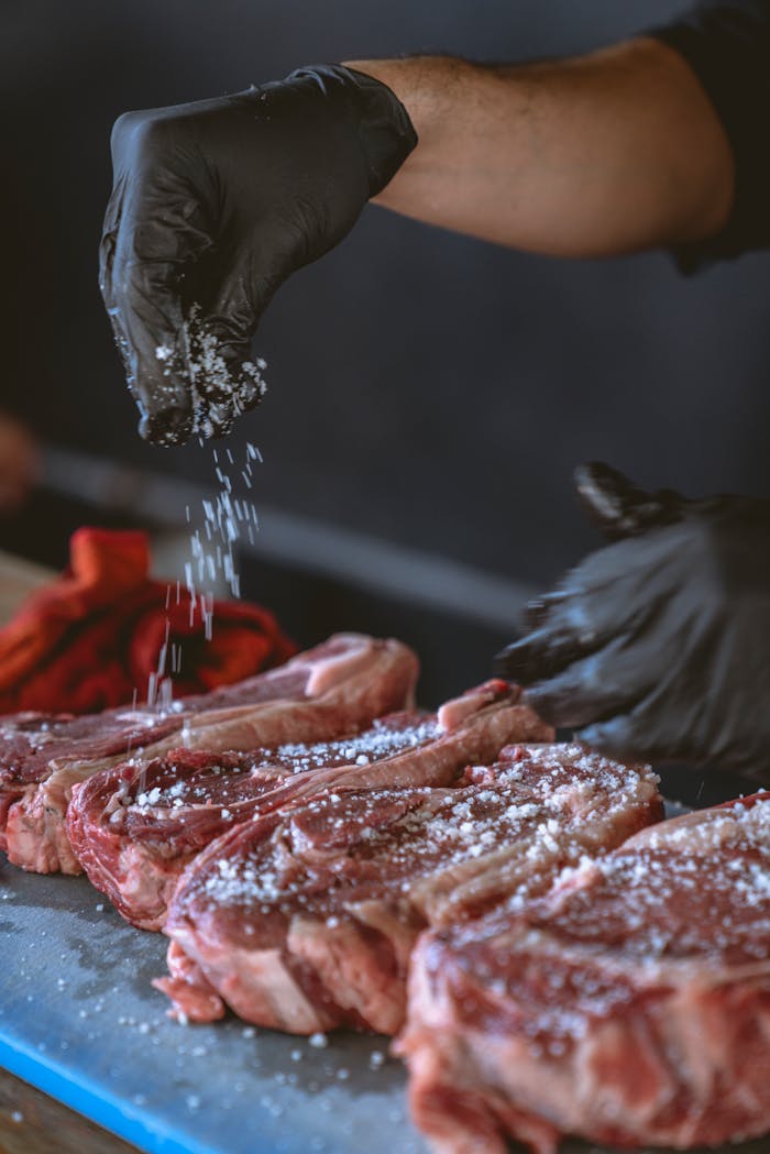 A chef seasons raw steaks with sea salt, perfecting the preparation process.